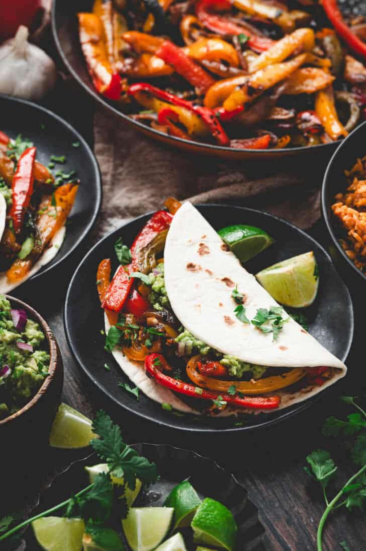 Tortillas filled with fajita peppers in a dinner table scene with Mexican rice and guacamole.