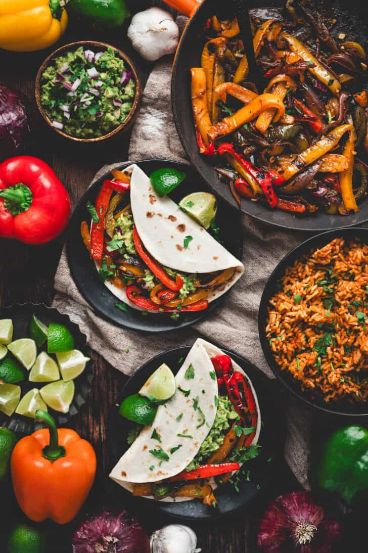 Tortillas filled with fajita veggies in a dinner table scene with Mexican rice and guacamole.