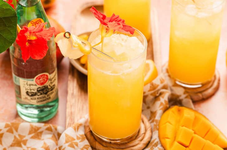 A mango lemon drink in a glass, garnished with an orange flower.