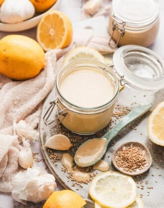 A small jar of lemon tahini dressing surrounded by the ingredients used to make it.