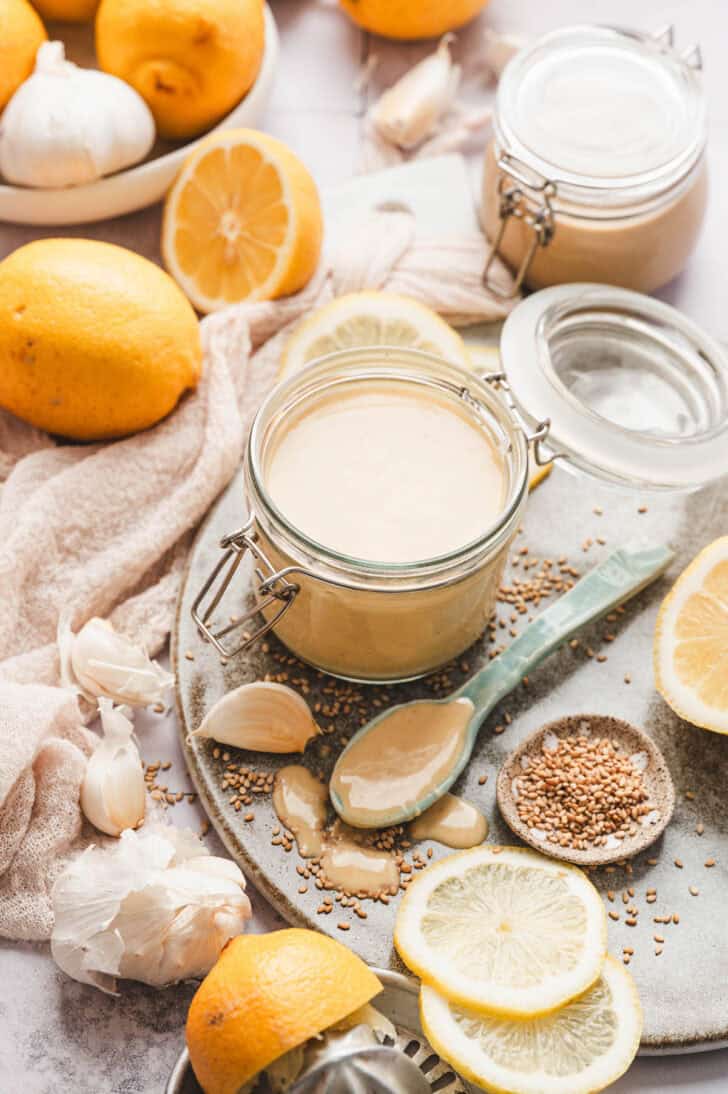 A small jar of lemon tahini dressing surrounded by the ingredients used to make it.