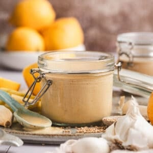 A small jar of lemon tahini dressing surrounded by the ingredients used to make it.