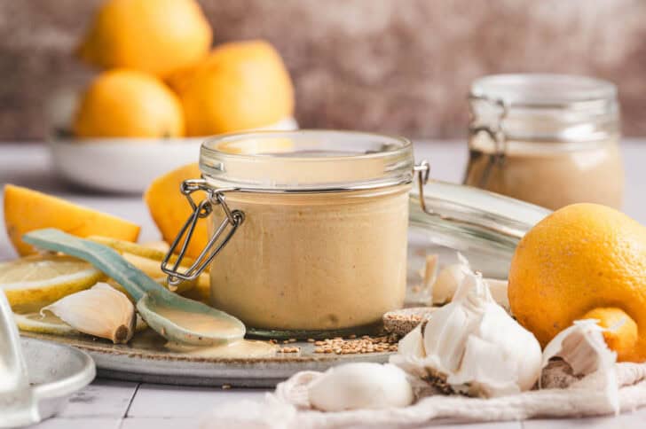 A small jar of lemon tahini salad dressing surrounded by the ingredients used to make it.