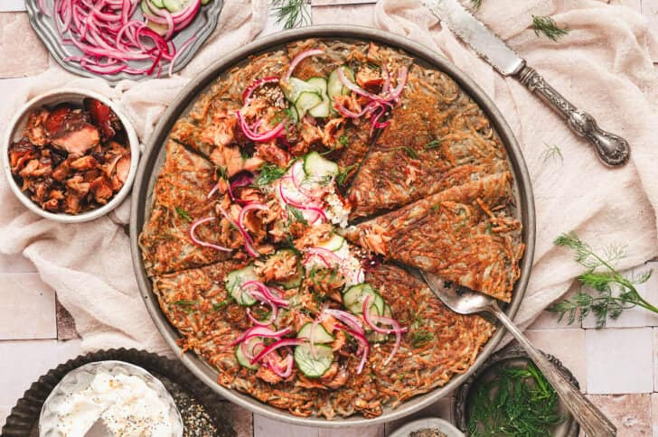 A pan of rosti potatoes topped with cream cheese, smoked salmon and pickled veggies.