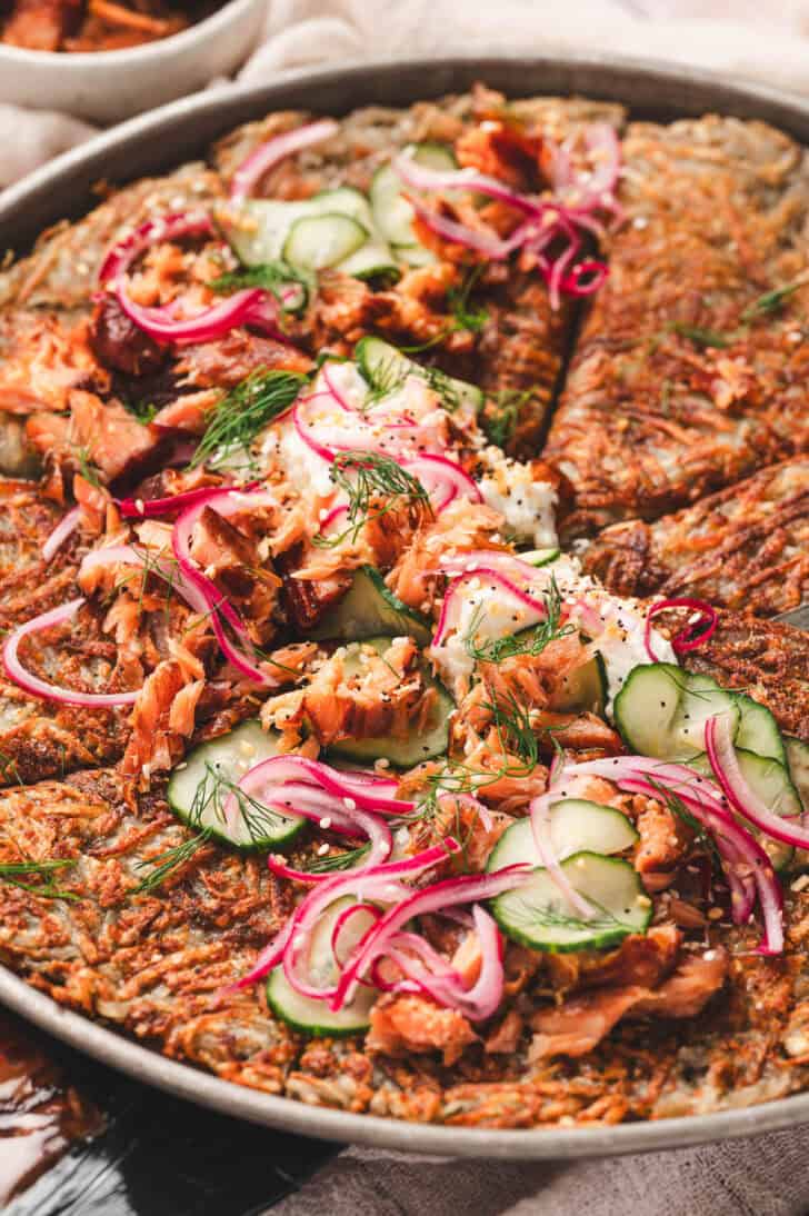 A rosti potato topped with cream cheese, salmon, cucumbers and onions.