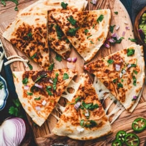 A shrimp quesadilla recipe on a wooden cutting board, surrounded by condiments.