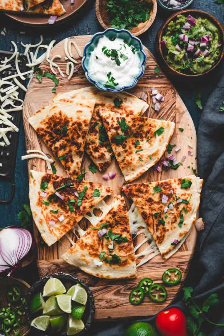 A shrimp quesadilla recipe on a wooden cutting board, surrounded by condiments.