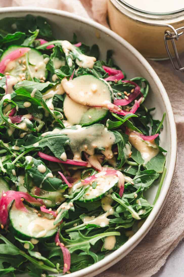 A salad made with greens, cucumbers and red onion drizzled with a lemon tahini dressing recipe.