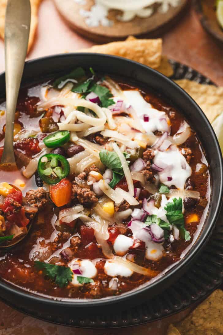A bowl of a crockpot taco soup recipe surrounded by toppings for it.