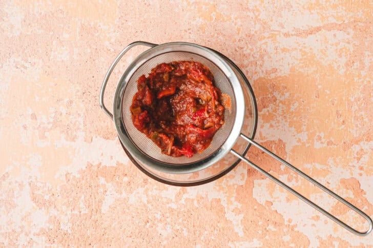 Salsa in a fine mesh strainer set over a bowl.