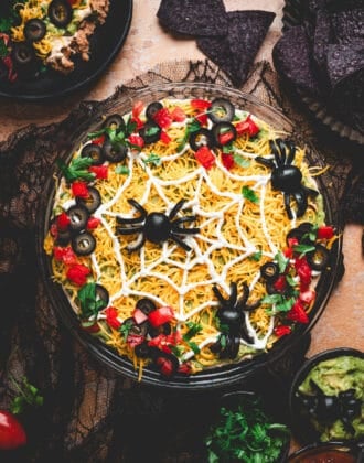 A round dish of Halloween dip topped with black olive spiders.
