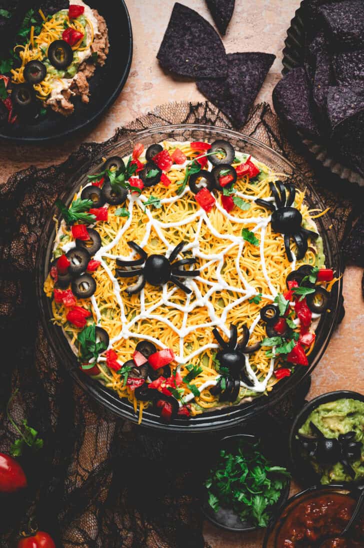 A round dish of Halloween dip topped with black olive spiders.