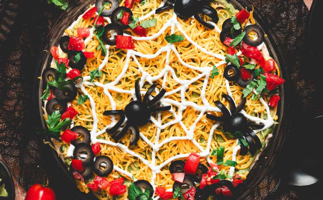 A round dish of Halloween dip topped with black olive spiders.