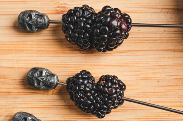 Two cocktail skewers with two blackberries each on them.