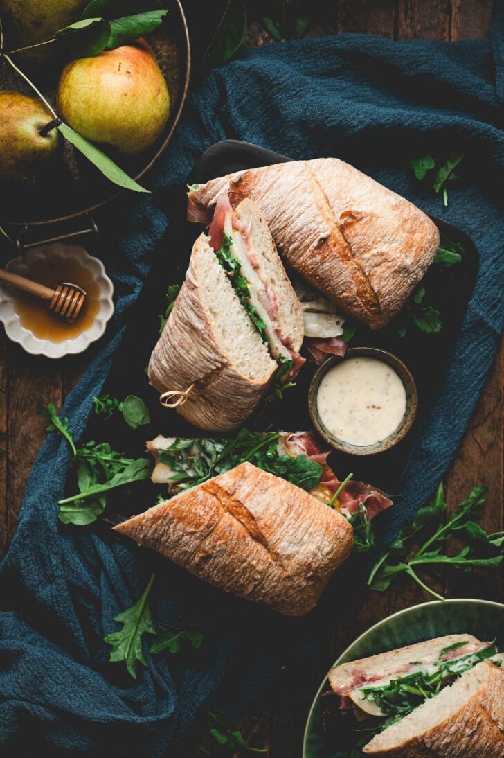 An Italian prosciutto sandwich on a dark background with ingredients surrounding it.