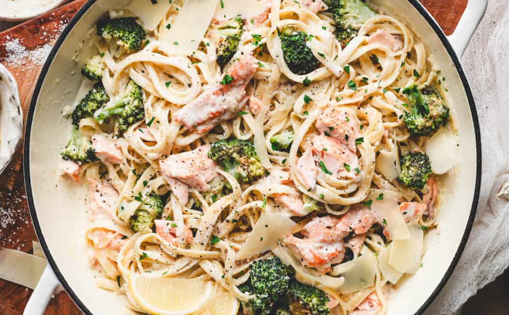 A white dutch oven filled with salmon alfredo.