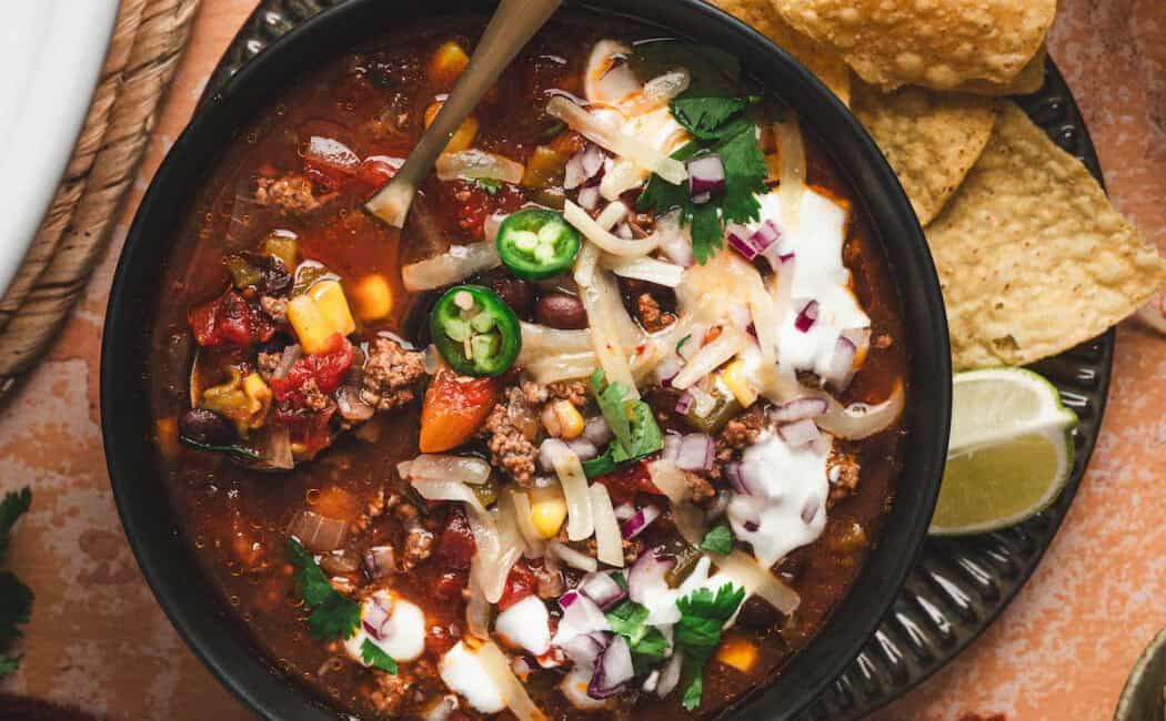 A bowl of slow cooker taco soup surrounded by toppings for them.