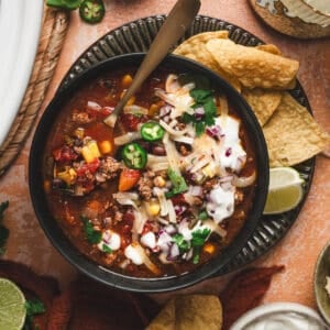 A bowl of slow cooker taco soup surrounded by toppings for them.