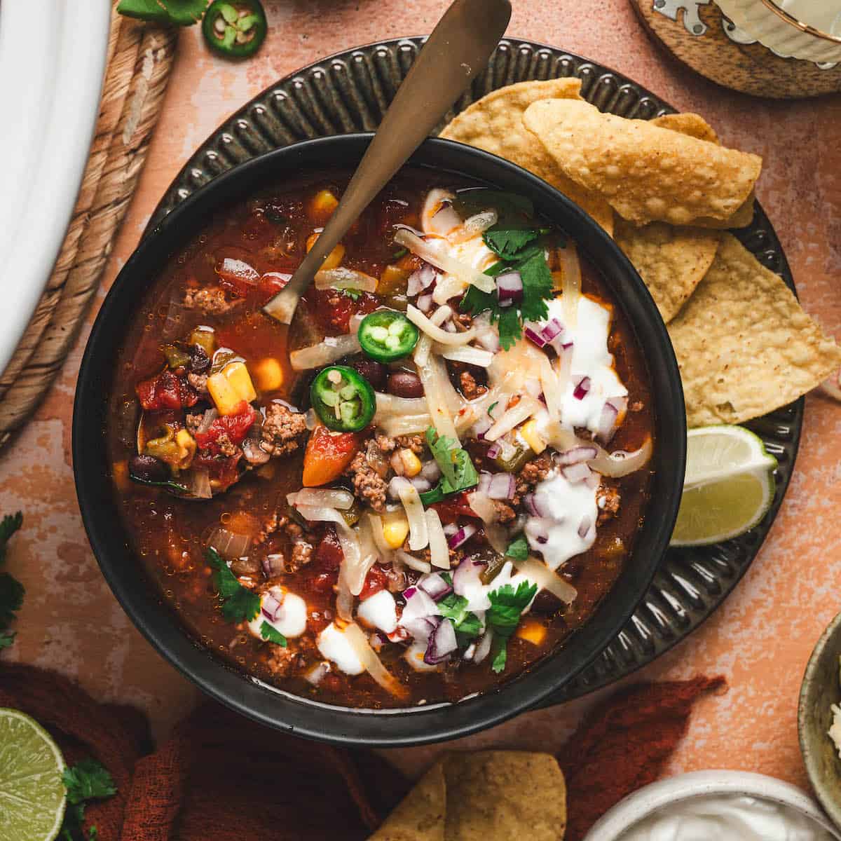 A bowl of slow cooker taco soup surrounded by toppings for them.