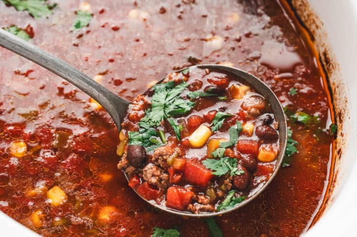 A ladle lifting a serving of crockpot taco soup.