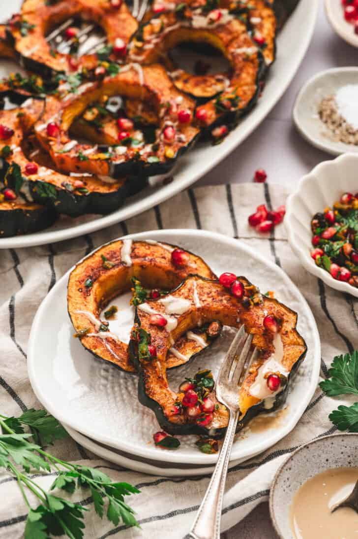 Two baked acorn squash slices with toppings on a small white plate.