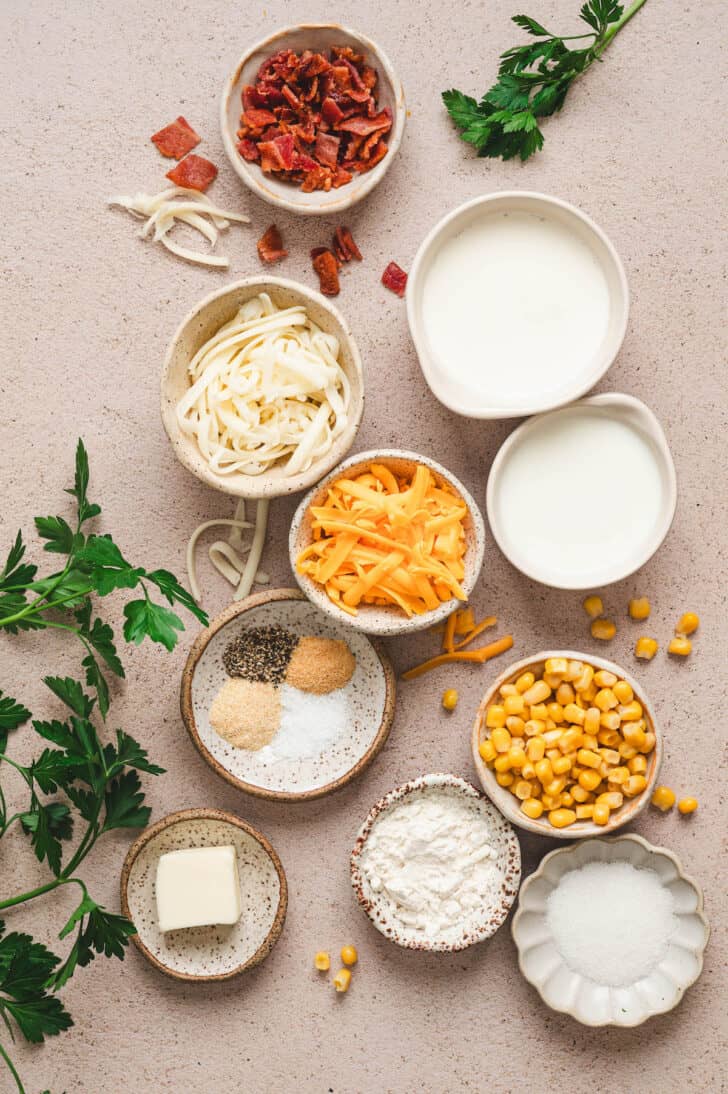 Ingredients, mostly in bowls, on a light background, including corn, cheese, dairy, spices and bacon.