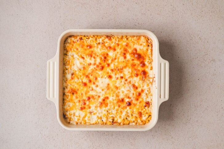 A corn casserole with cheese in a square baking dish.