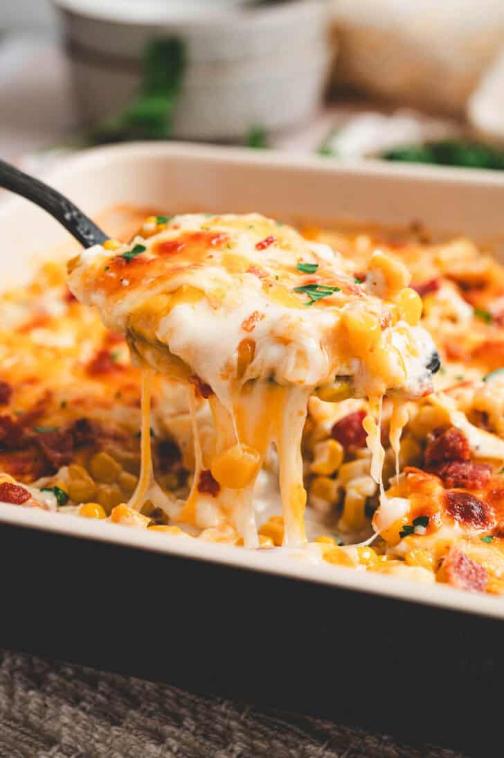 A spoon lifting a scoop of cheesy corn casserole from a baking dish.