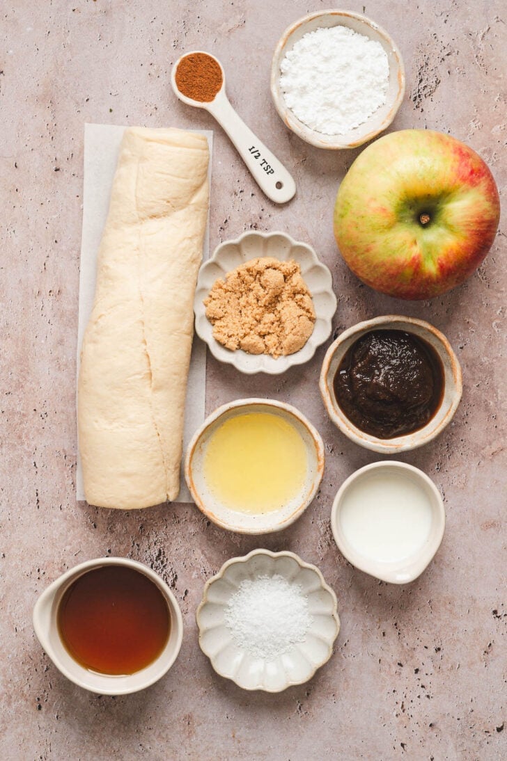 Ingredients on a light surface, including pastry dough, apples, butter and spices.