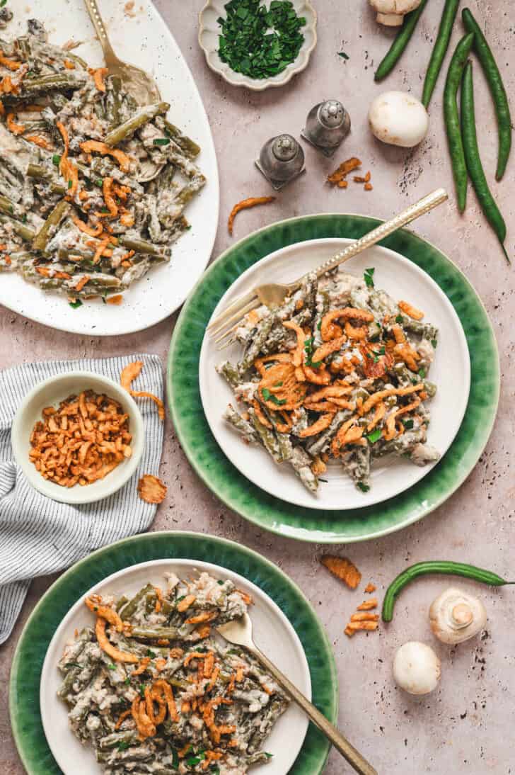 Two plates and a platter filled with fresh green bean casserole in crock pot.