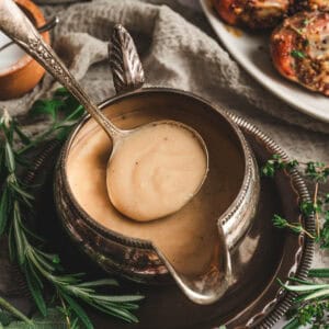 A pewter gravy boat filled with gravy from scratch, with a spoon lifting some out.