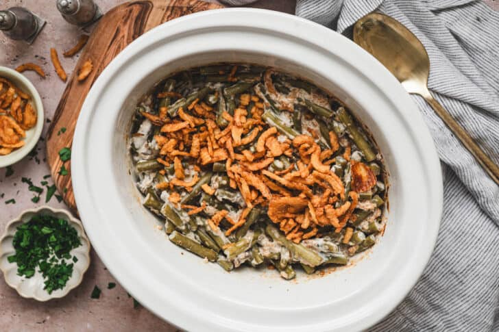A white crock pot bowl filled with slow cooker green bean casserole with fresh green beans.