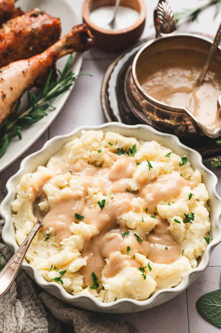 Scalloped edged white bowl filled with mashed potatoes with heavy cream topped with gravy.
