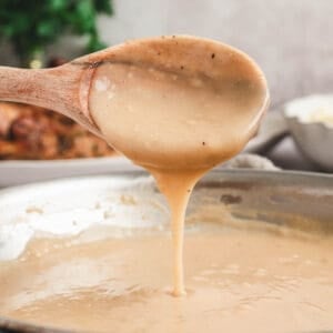 A wooden spoon drizzling a gravy recipe from a skillet.