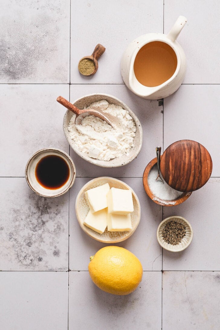 Ingredients on a light tiled surface, including butter, lemon, flour and spices.