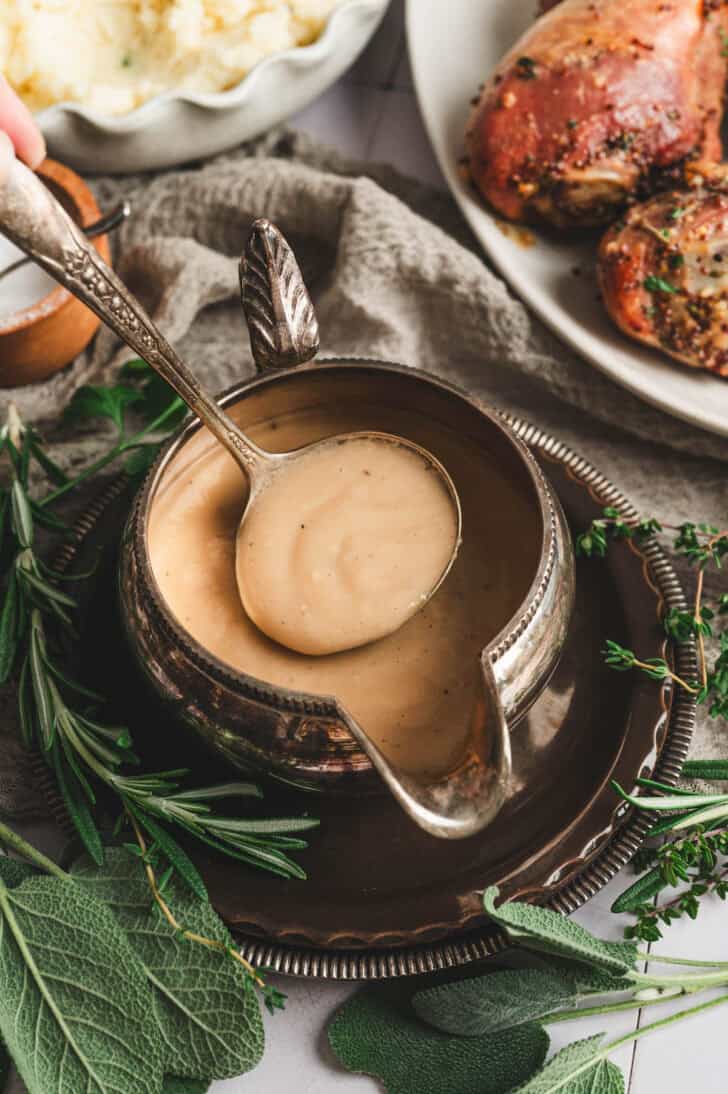 A pewter gravy boat filled with a turkey gravy recipe, with a spoon lifting some out.