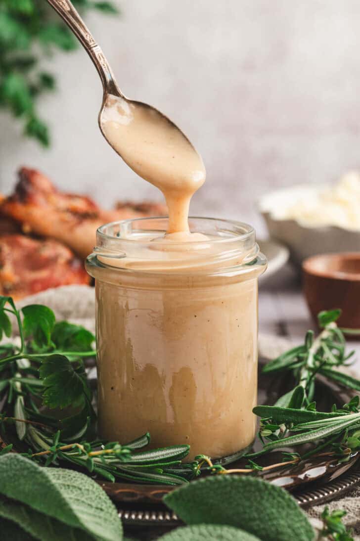A spoon drizzling homemade turkey gravy into a glass jar.