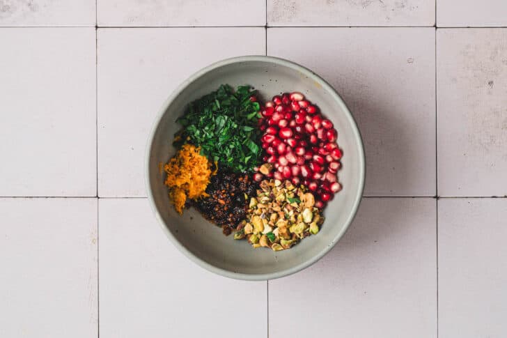 A bowl filled with pomegranate arils, parsley, pistachios, orange zest and chili crisp.