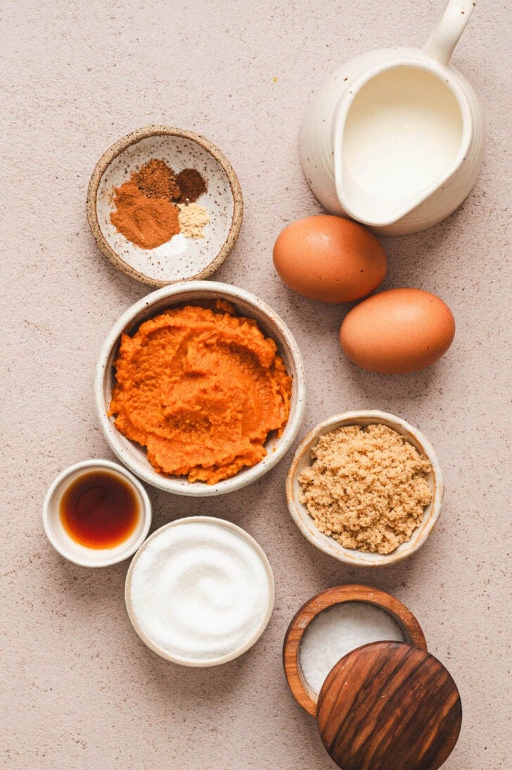 Ingredients on a light surface, including pureed squash, eggs, sugar, dairy and spices.