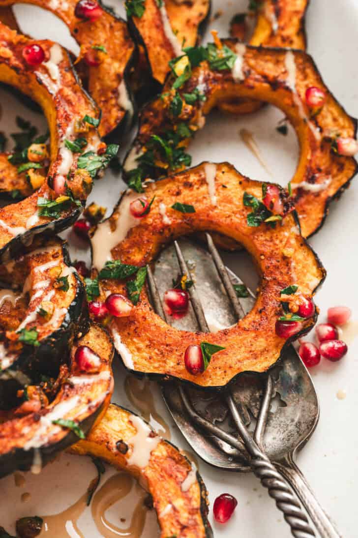 A fork scooping a serving of acorn squash roasted slices from a platter.