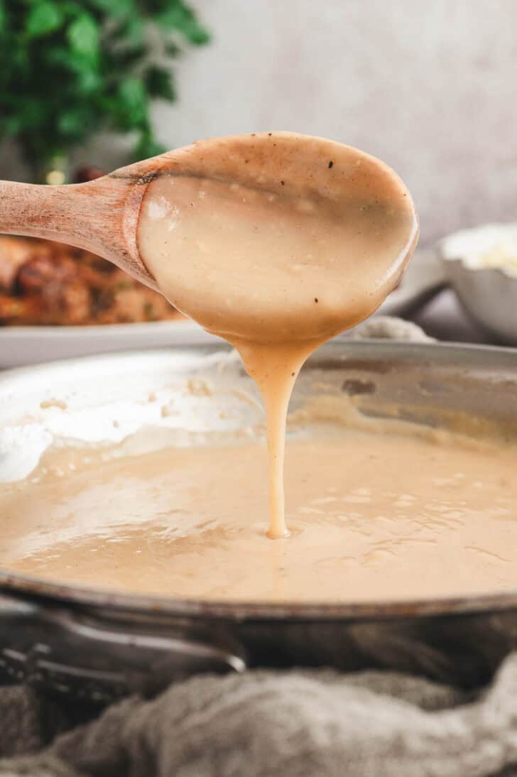 A wooden spoon drizzling a gravy recipe from a skillet.
