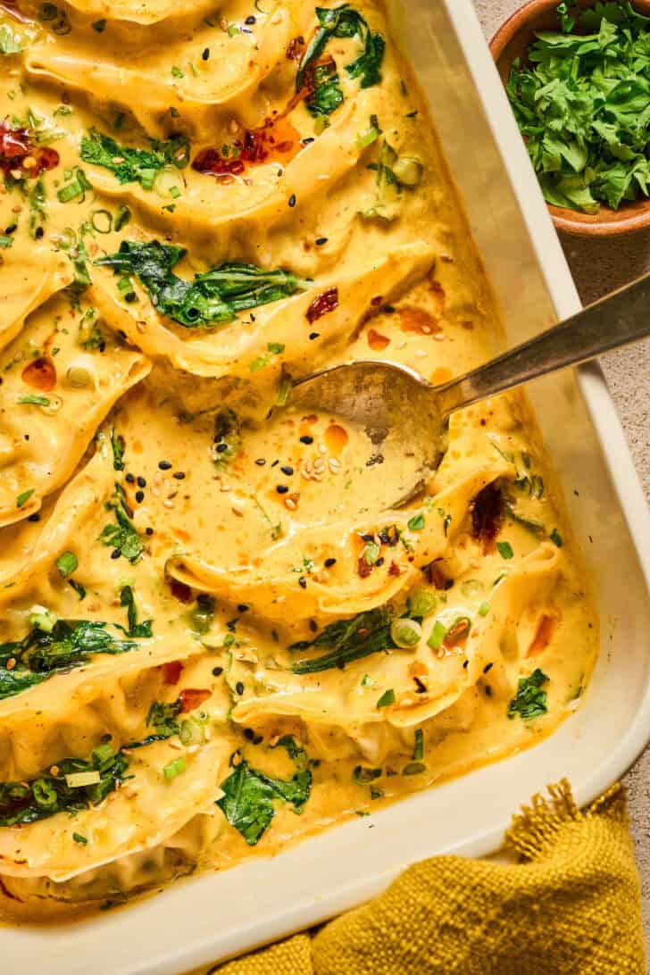 A spoon dipping into a baking dish of one pan dumpling dinner.