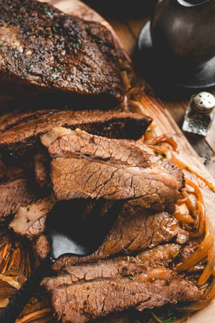 The result of cooking brisket in the oven, being sliced on a wooden board.