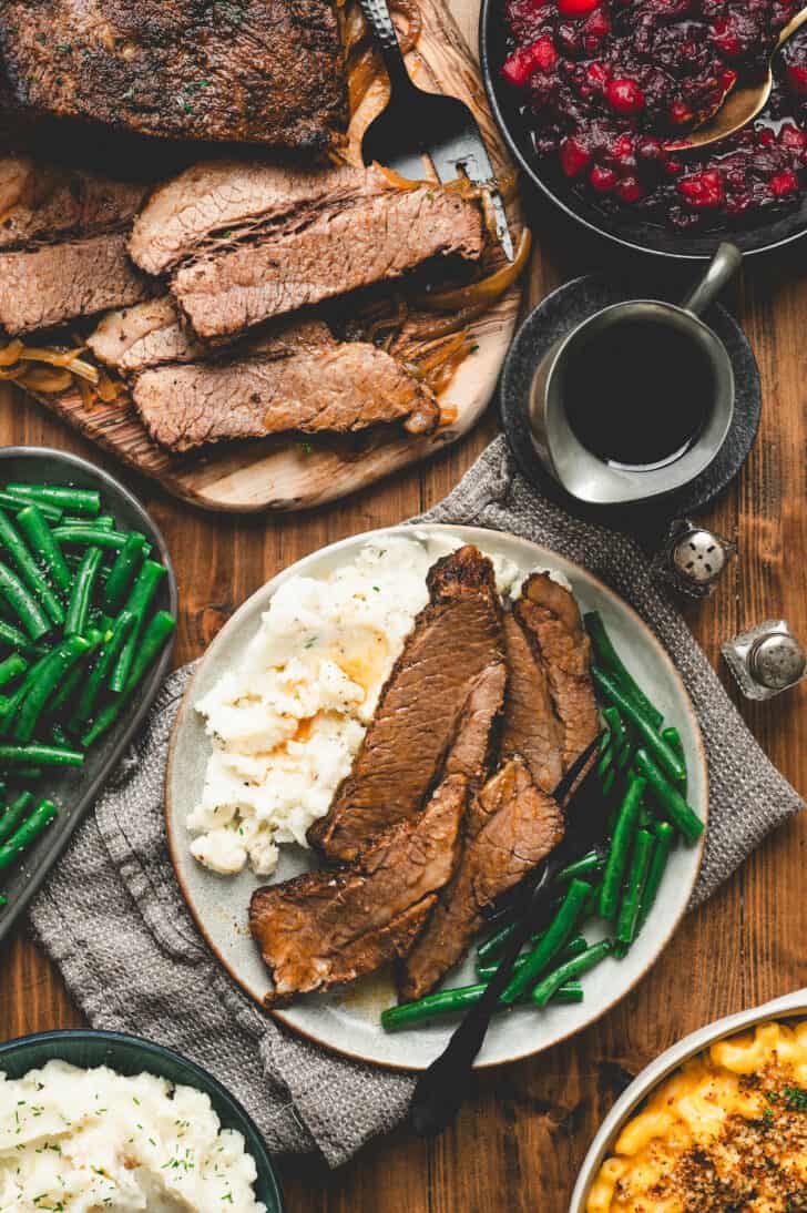 A holiday dinner scene with beef brisket in the oven and festive side dishes.