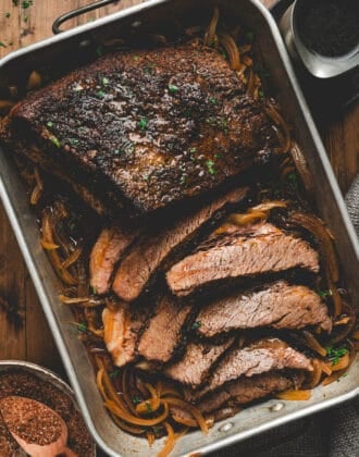 A roasting pan full of brisket in the oven, with some of it sliced.