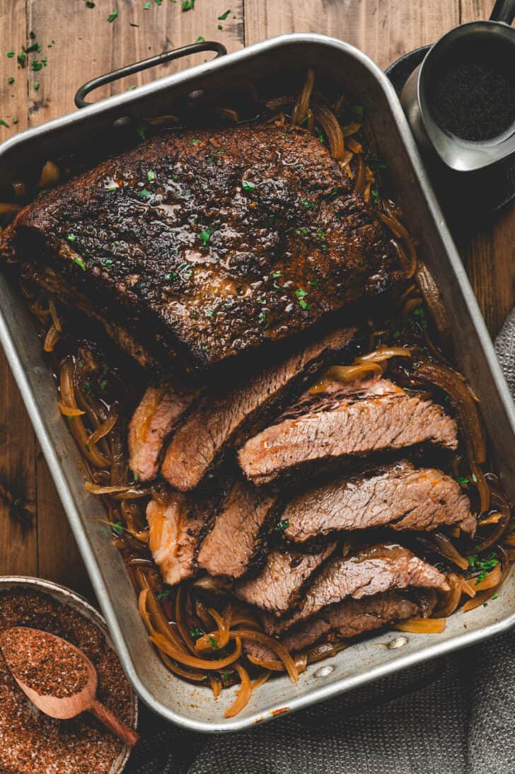 A roasting pan full of brisket in the oven, with some of it sliced.