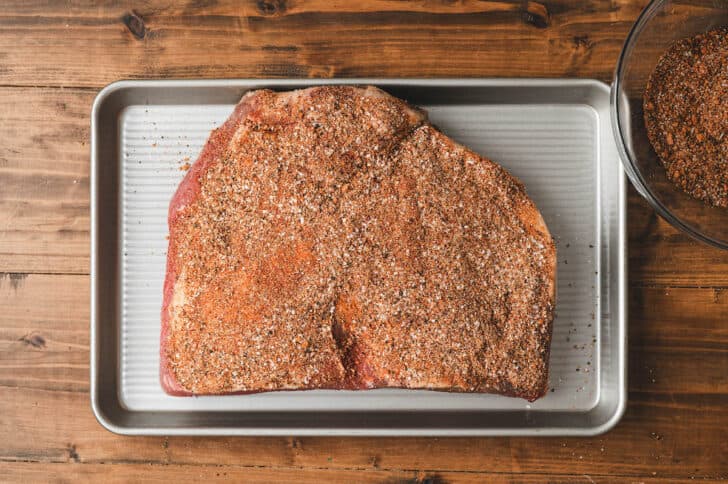 A brisket rubbed with spices on a sheet pan.