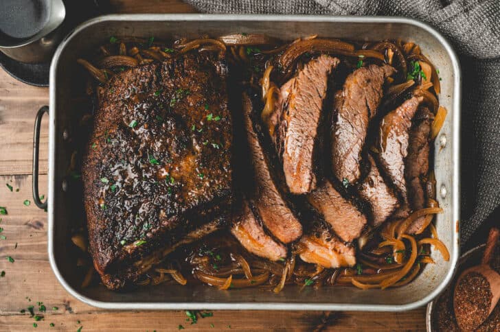A roasting pan full of a brisket in the oven recipe, with some of it sliced.