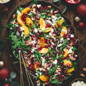 A large oval platter filled with Christmas salad, with serving utensils placed along the side.