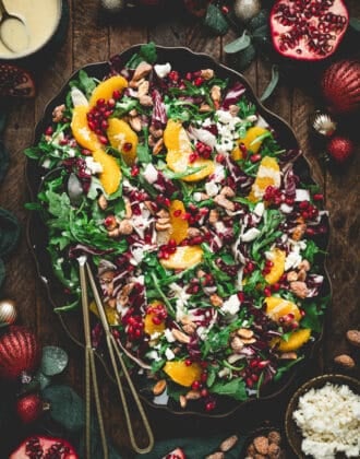 A large oval platter filled with Christmas salad, with serving utensils placed along the side.